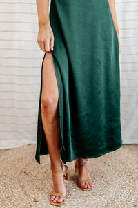Pictured is a green, silky midi dress with a v-neckline, adjustable shoulder straps, seamless side-zipper, and deep side slit.
