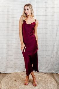 Pictured is a red, stunning and silky satin slip dress with a flattering cowl neckline, slit on the side, adjustable straps, and midi length.