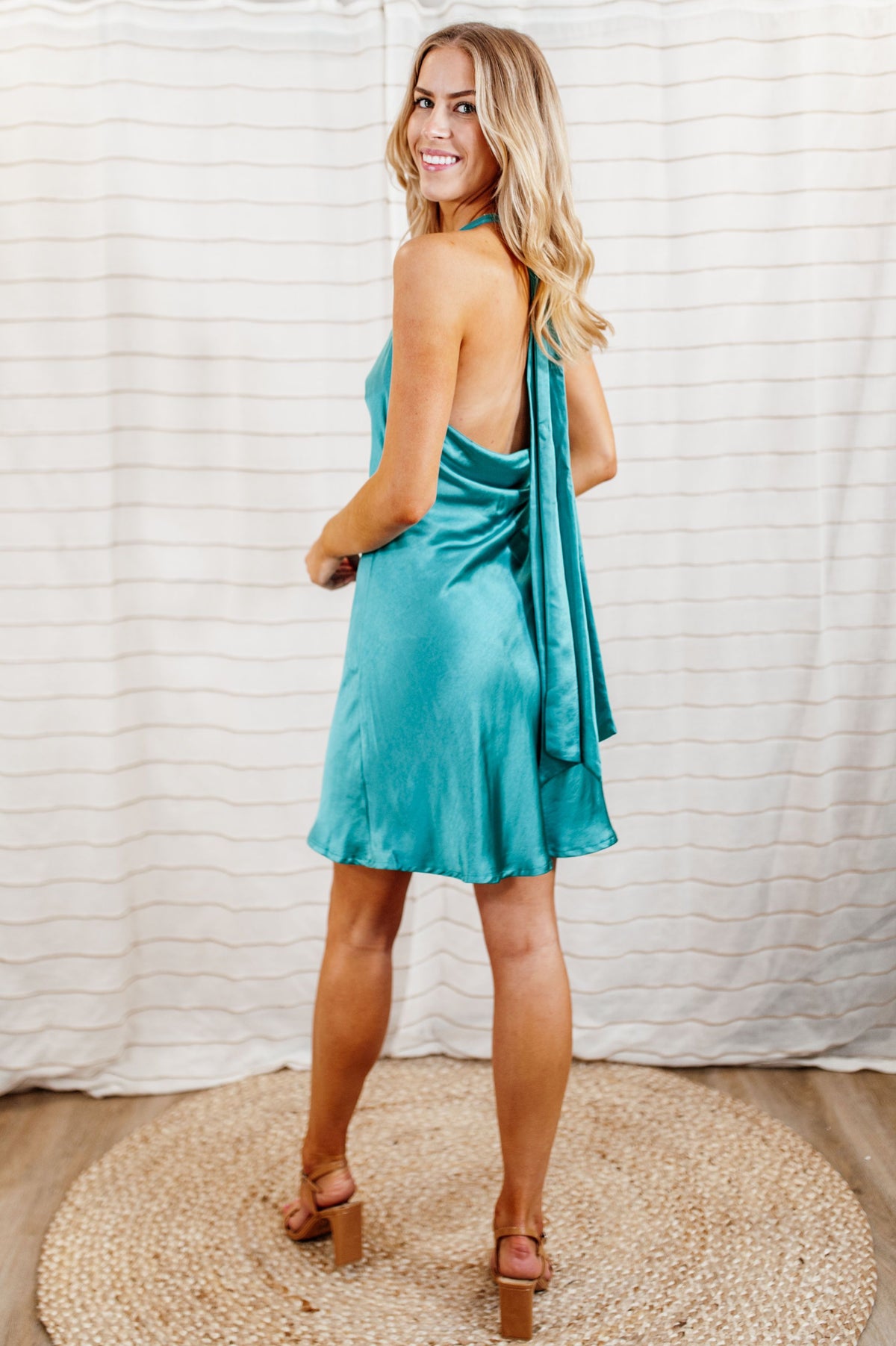 Bright teal, silky satin mini halter dress with cowl neck and flowy skirt on model.