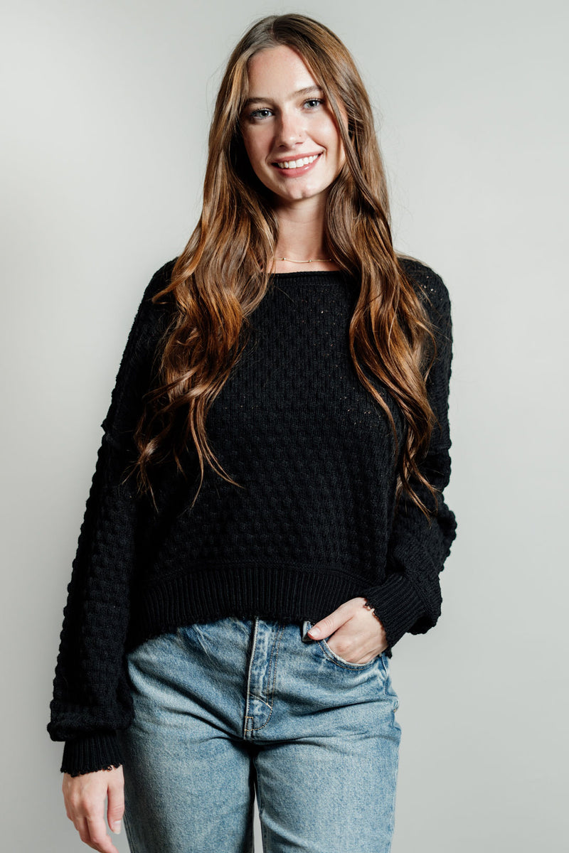 Pictured is a black, knit sweater with a scoop neckline, cropped body, and cuffed knit sleeves.