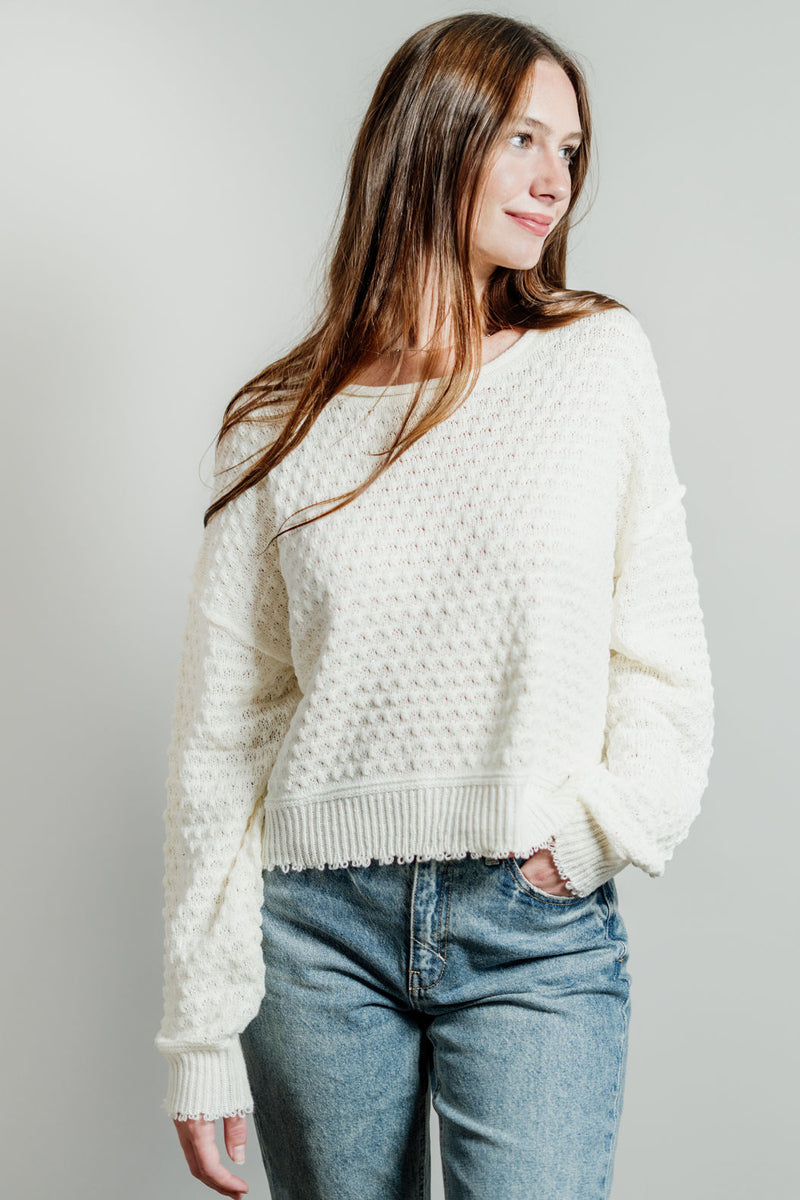 Pictured is a white, knit sweater with a scoop neckline, cropped body, and cuffed knit sleeves.