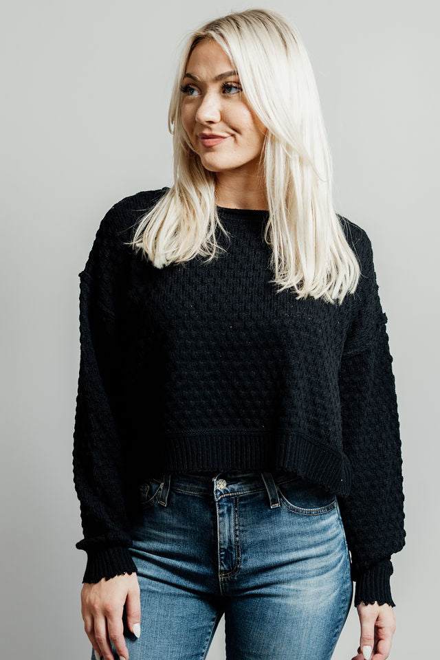 Pictured is a black, knit sweater with a scoop neckline, cropped body, and cuffed knit sleeves.