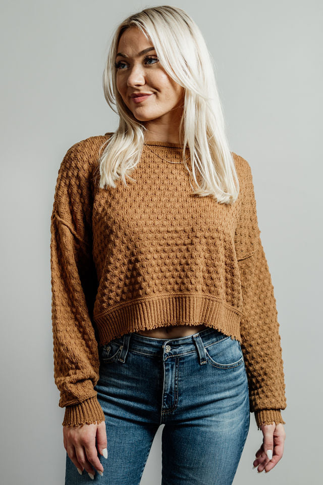 Pictured is a dark mustard-yellow, knit sweater with a scoop neckline, cropped body, and cuffed knit sleeves.