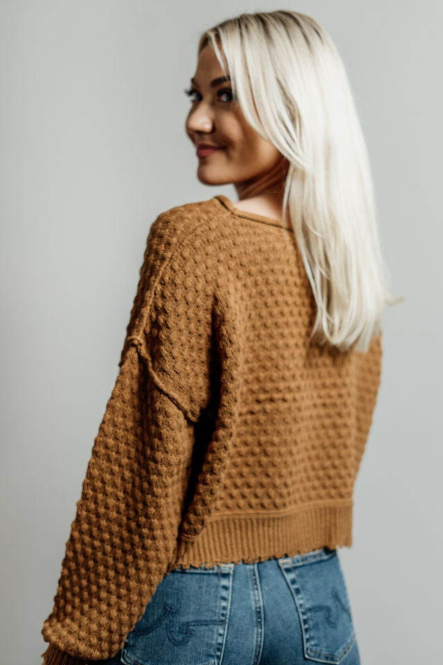 Pictured is a dark mustard-yellow, knit sweater with a scoop neckline, cropped body, and cuffed knit sleeves.