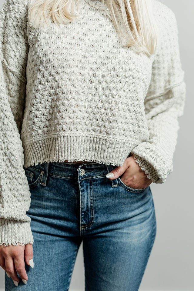 Pictured is an off-white, knit sweater with a scoop neckline, cropped body, and cuffed knit sleeves.