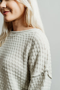 Pictured is an off-white, knit sweater with a scoop neckline, cropped body, and cuffed knit sleeves.