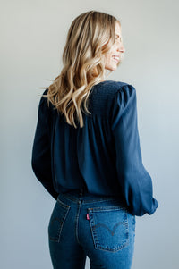 Pictured is a blue, flowy blouse with a v-neckline, balloon sleeves, and pleated back panel.