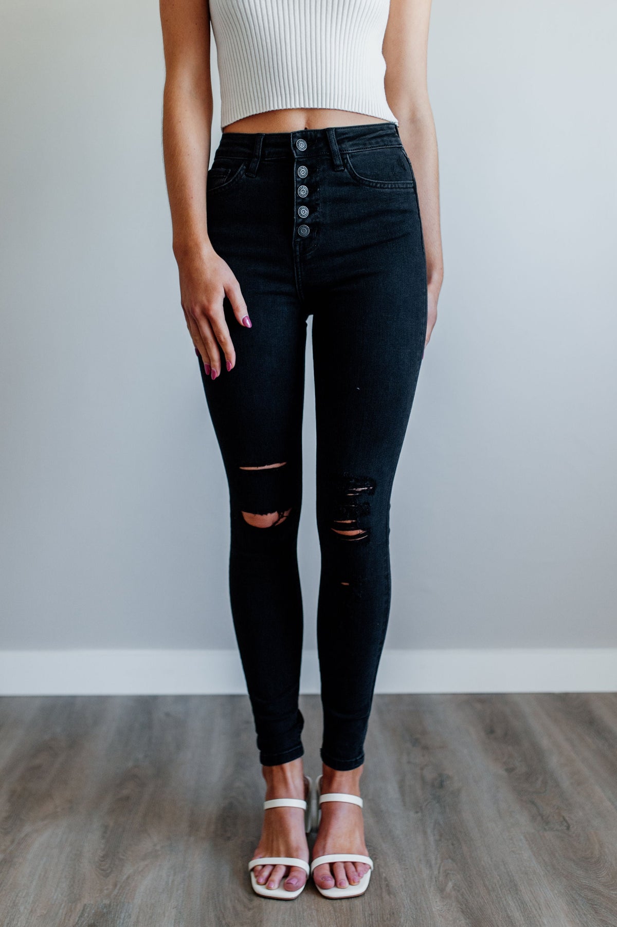 Pictured is a pair of black denim with a high-rise waist, button fly, and knee distressing on both legs. 