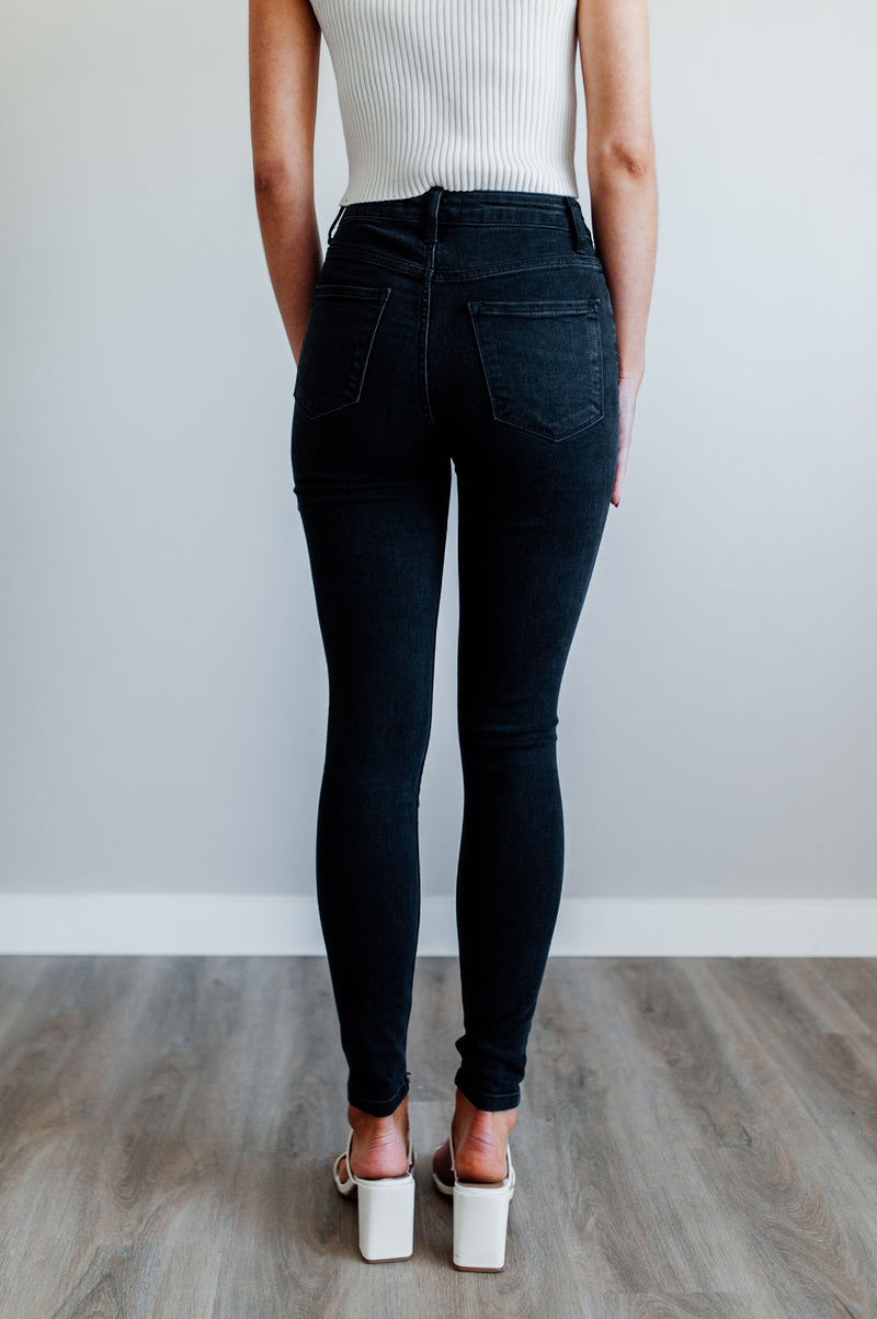 Pictured is a pair of black denim with a high-rise waist, button fly, and knee distressing on both legs. 