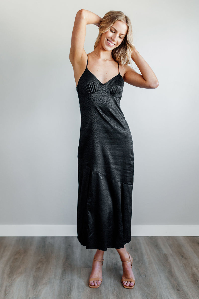 Pictured is a black satin dress with a v-neckline, adjustable straps, and subtle animal print.