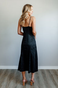 Pictured is a black satin dress with a v-neckline, adjustable straps, and subtle animal print.