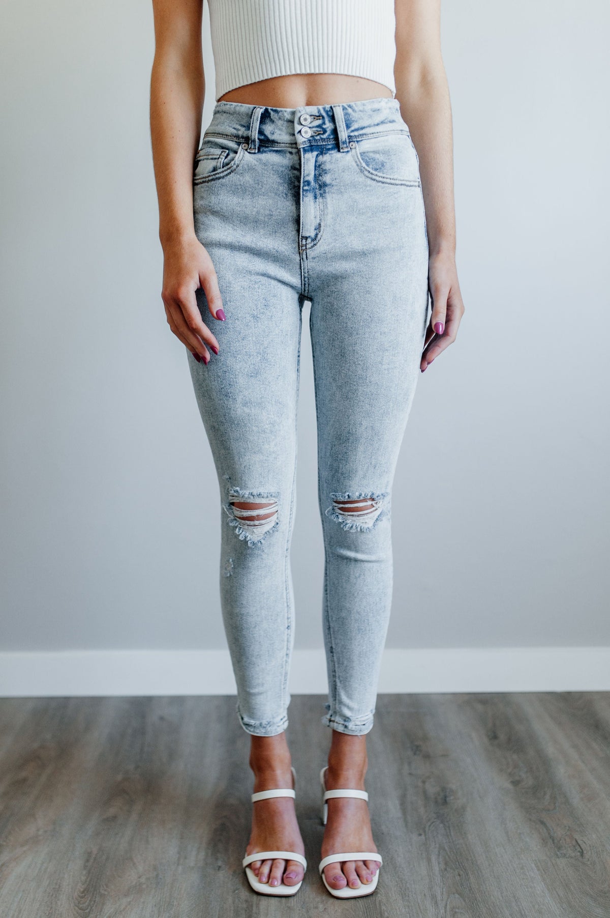 Pictured is a trendy high rise, denim jean with updated acid-wash material, light distressing, and cropped ankle.
