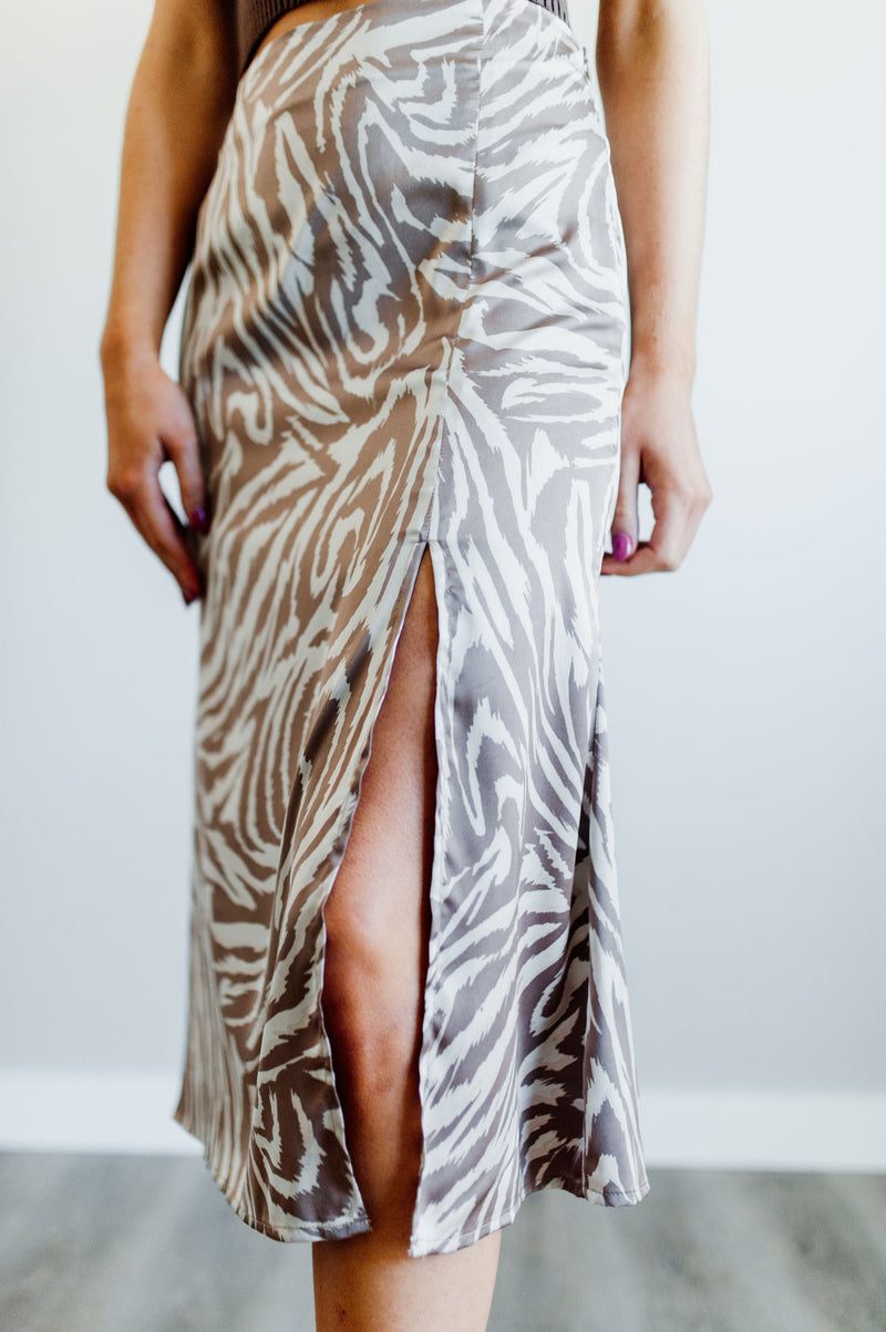 Pictured is a brown and beige zebra-print, slip skirt with a neutral zebra pattern placed on a silky skirt with side slit.