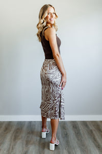 Pictured is a brown and beige zebra-print, slip skirt with a neutral zebra pattern placed on a silky skirt with side slit.