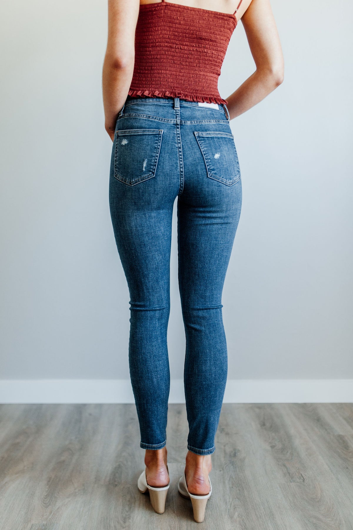 Pictured is a mid-wash, distressed denim jean with a high-rise waist, cropped ankles, and lightly distressed denim material.
