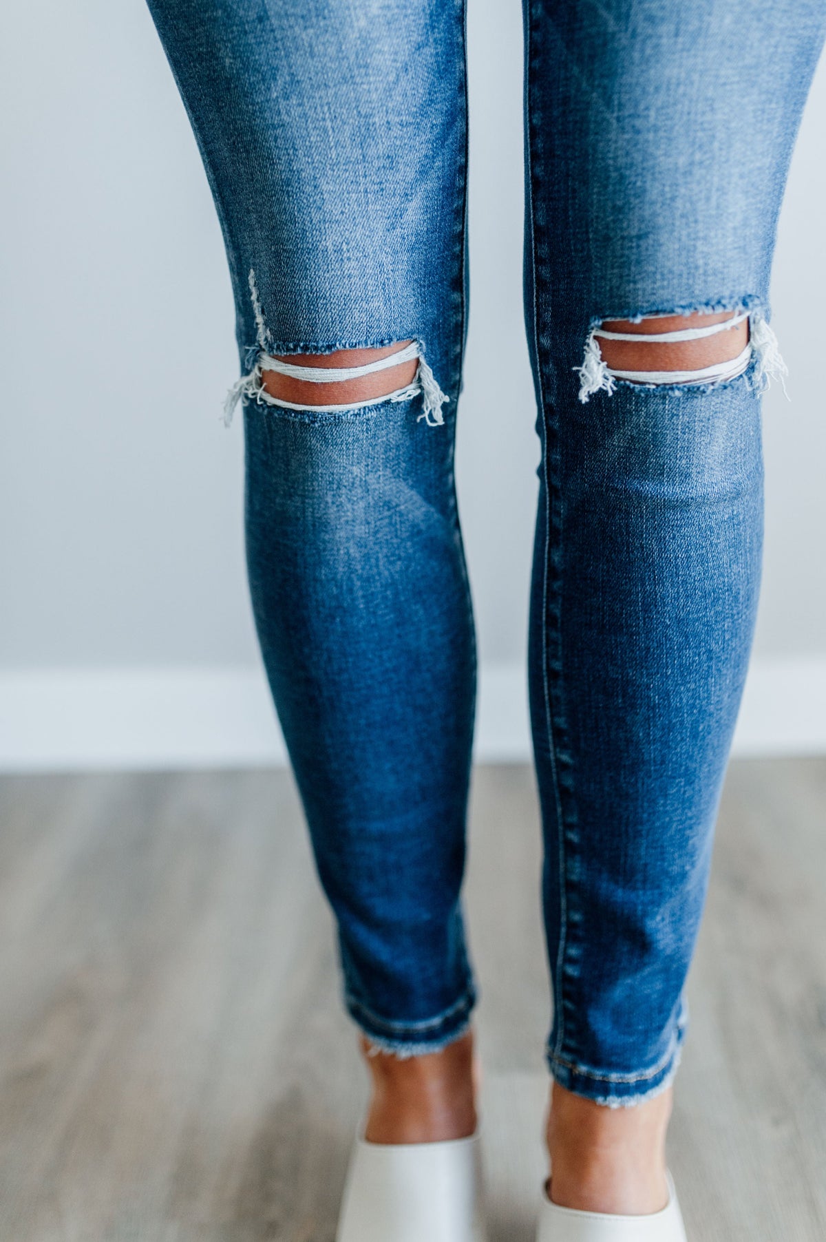 Pictured is a mid-wash, pair of denim with a mid-rise waist, medium-wash, knee slits, and cropped ankle with distressed hem.