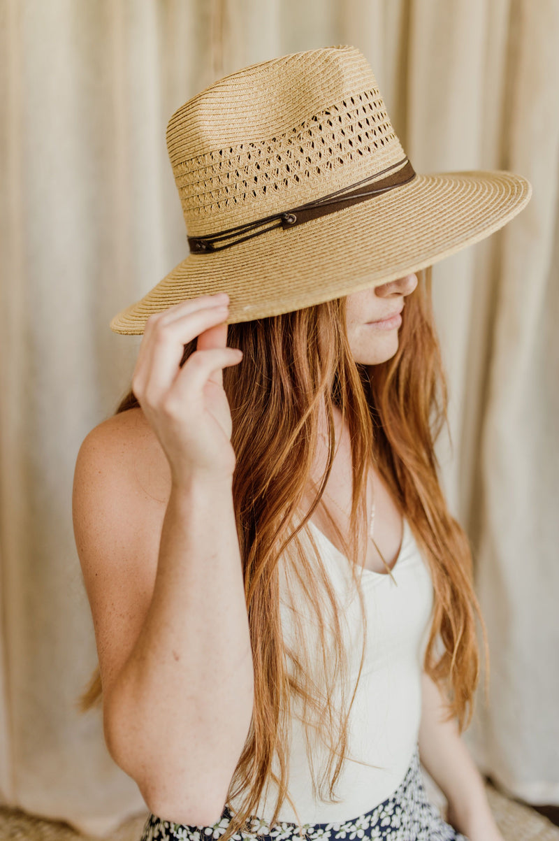 Pictured is a fedora-inspired sun hat comes in a tan color and features a fashionable brown leather-like band.