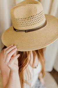 Pictured is a fedora-inspired sun hat comes in a tan color and features a fashionable brown leather-like band.
