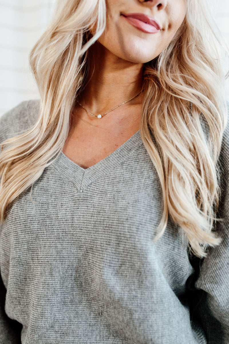 Pictured is a gray jersey pullover with a plush knit material, cuffed sleeves, cropped body, and v-neckline.